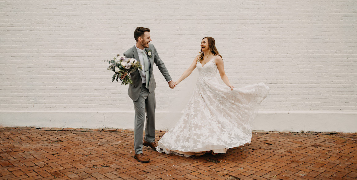 Groom holding bouquet while bride twirls her dress