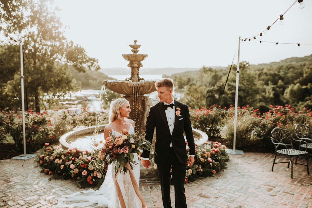 Bride and groom walking in front of floral fountain