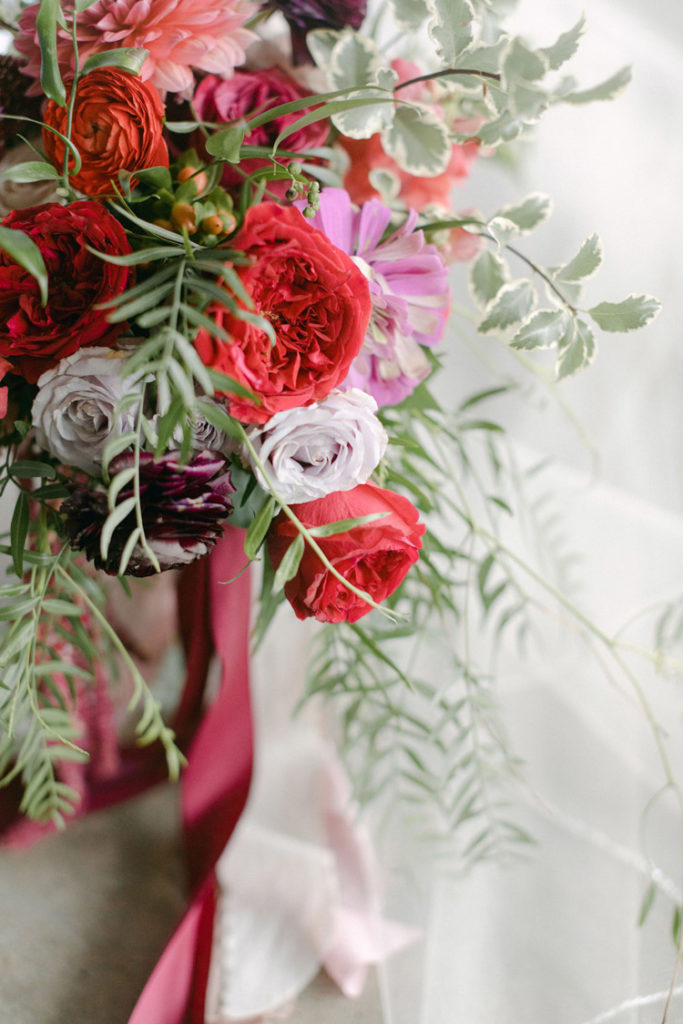 Close up of bridal bouquet with red garden roses, purple ranunculus, and pink cosmos
