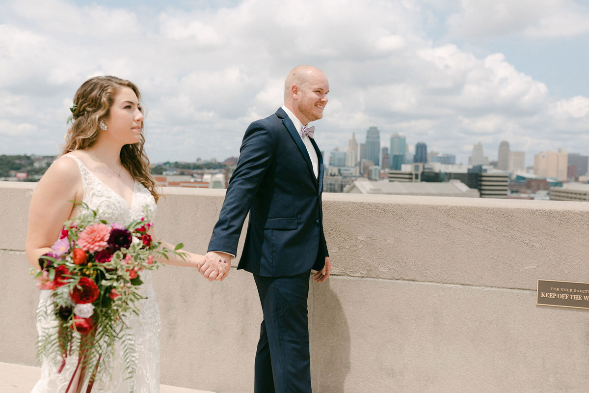 Bride and Groom walking hand in hand with KC skyline in the distance