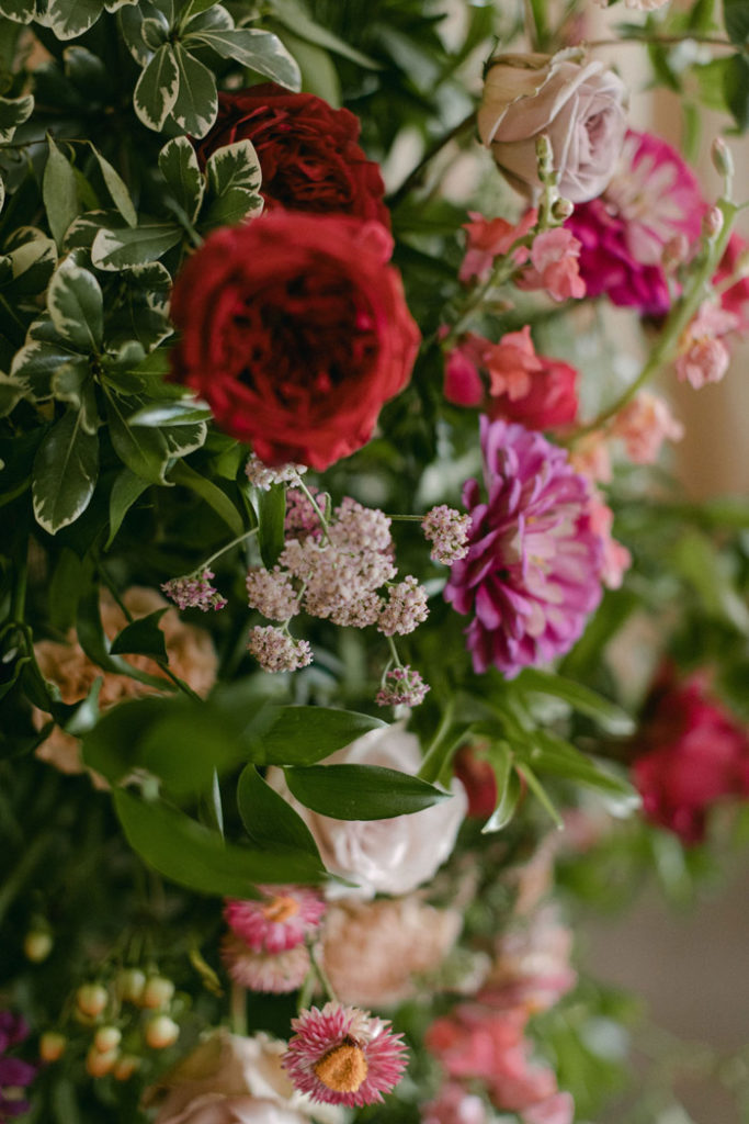Close up of berry tone flowers such as garden roses, zinnias, yarrow, and strawflower
