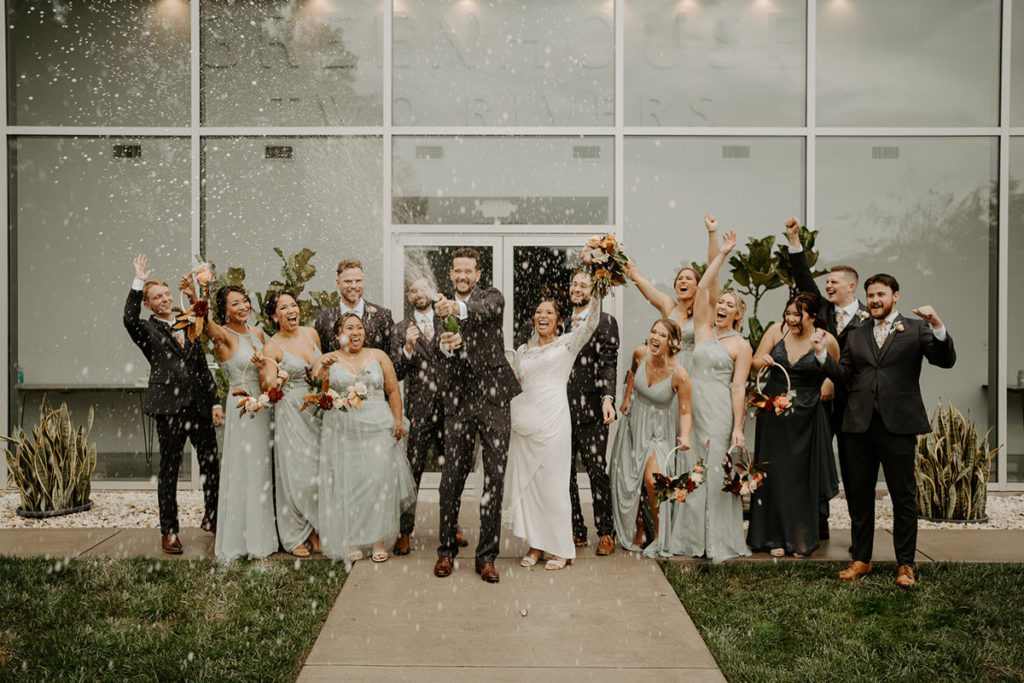 Wedding party celebrating while groom pops champagne