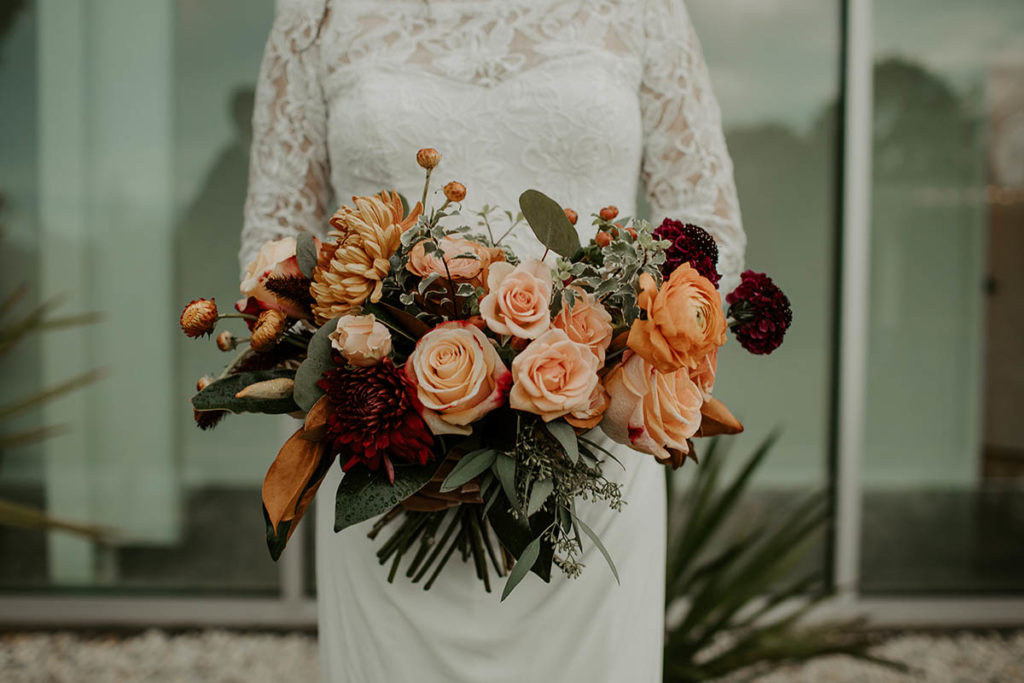 Close up of bridal bouquet featuring peach to burgundy fall wedding flowers
