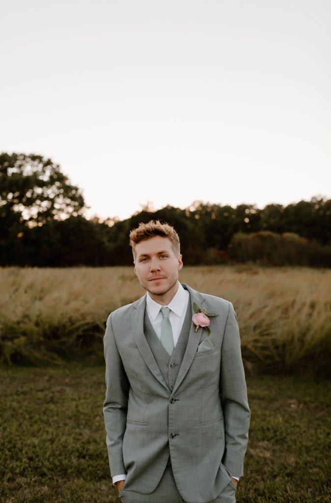 Groom standing in a field, looking at the camera with boutonniere on his suit