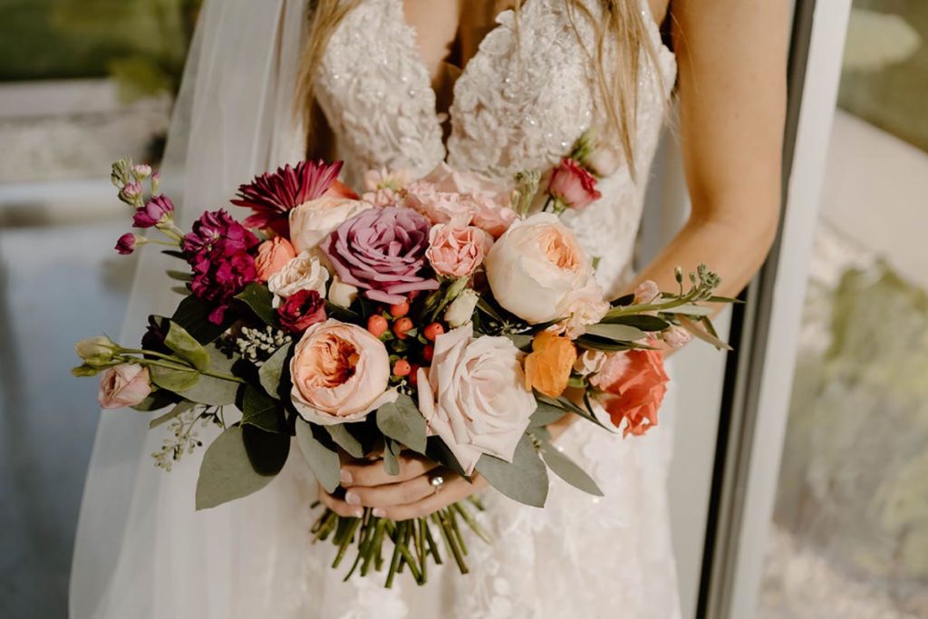 Close up of bride holding purple, peach, and pink wedding flowers