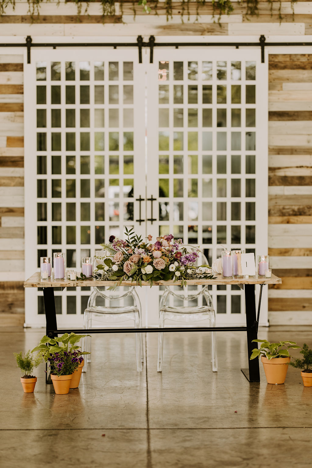 Sweetheart table with purple arrangement and potted plants resting on the floor