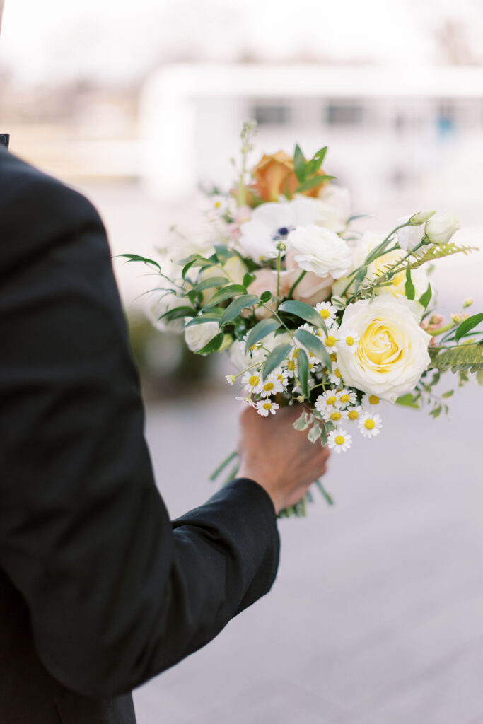 Side shot of the groom holding the bridal bouquet with white roses and chamomile