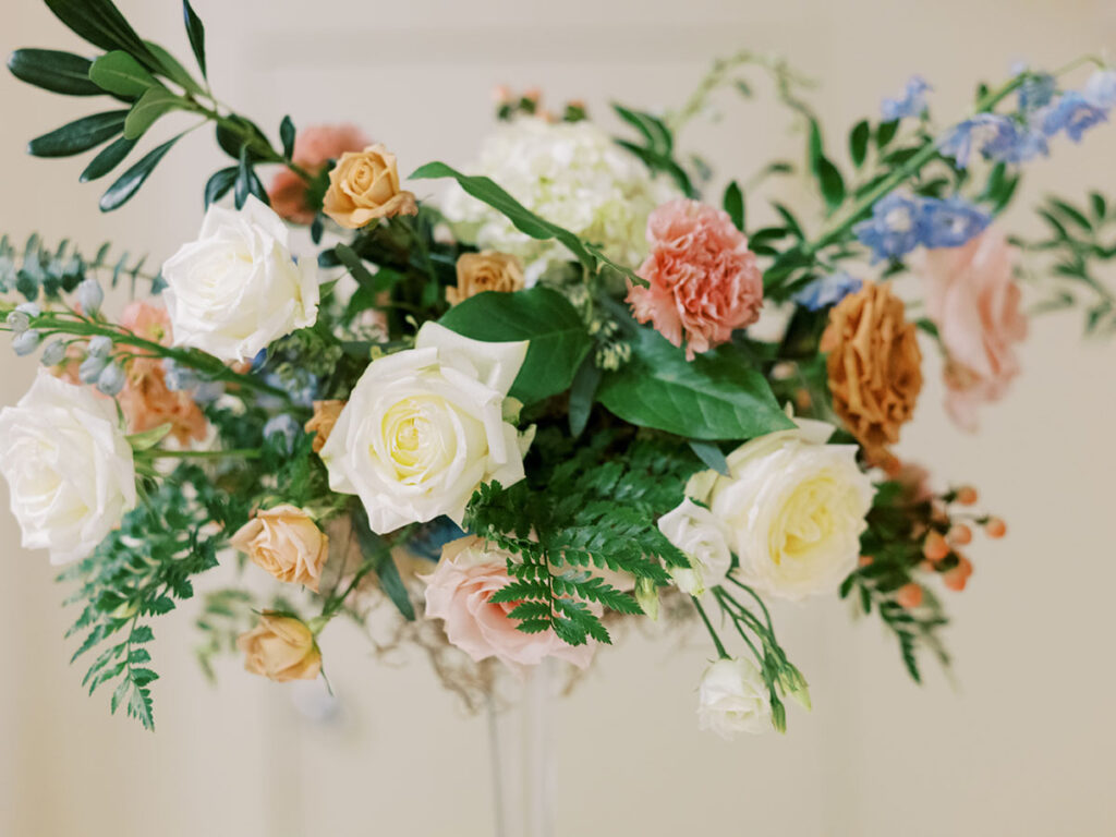 Tall floral arrangement with muted pinks, whites, toffees, and blue