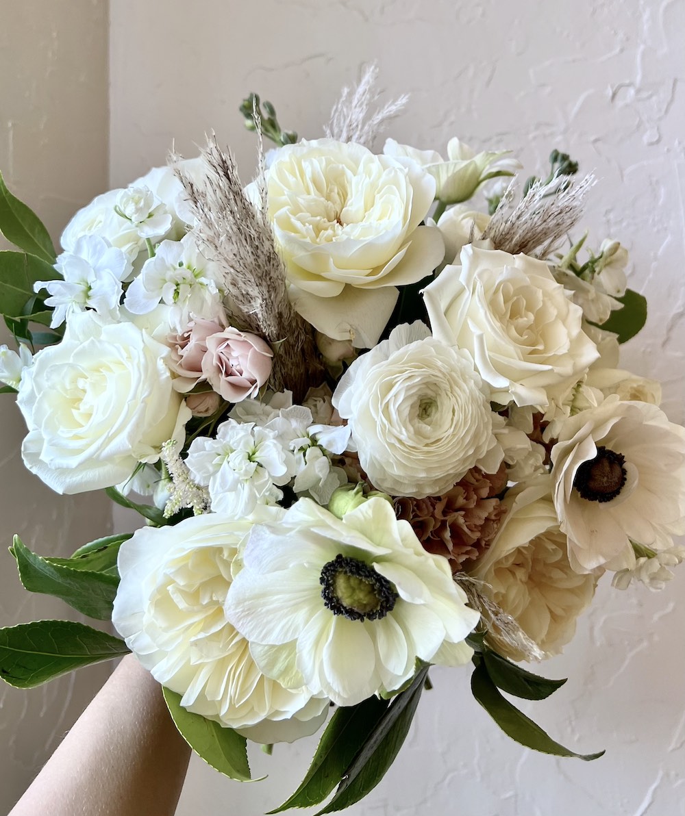 Arm holding  a mostly white bouquet with pops of light pink