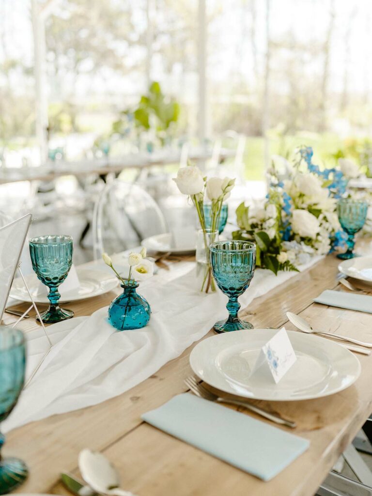 Blue goblets, bud vase, and napkins decorating the tables alongside the flowers.