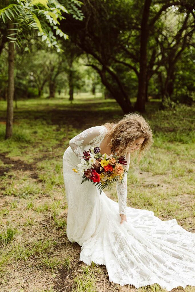 Bride fixing her train, holding woodsy wedding bouquet