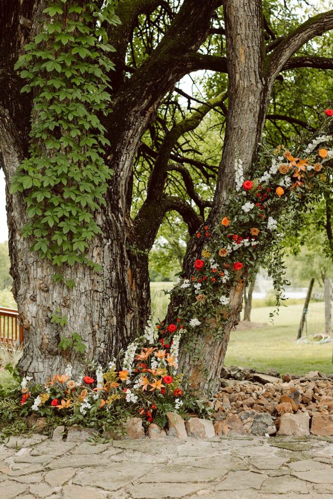 Floral installation with red, yellow, and orange flowers climbing up a large tree.