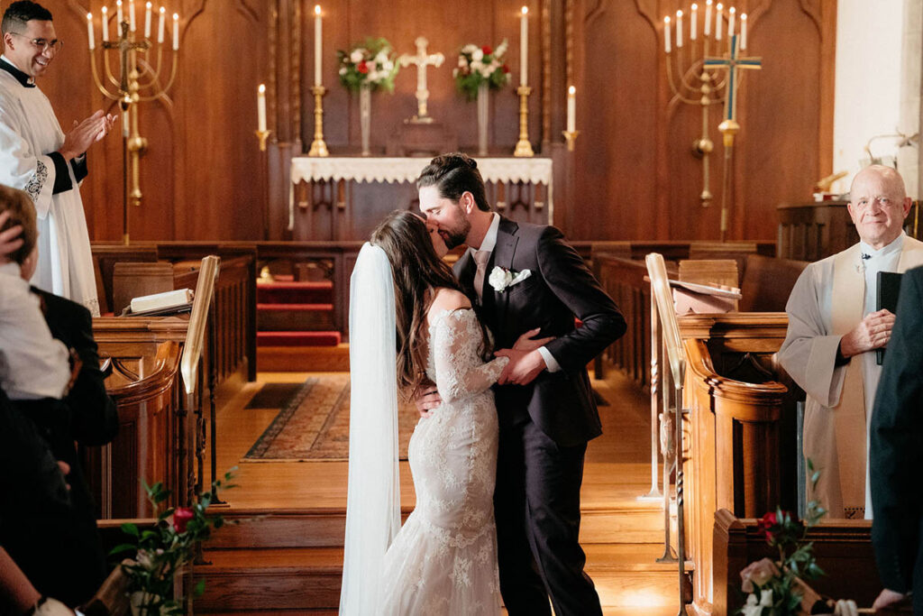 Couple shares first kiss during their ceremony with florals behind the altar
