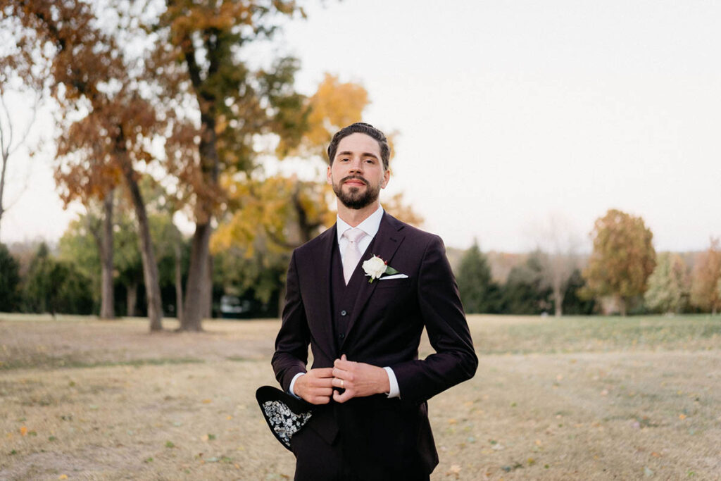 Groom wearing suit with fall background, wind blows bottom of jacket open to reveal black and white floral pattern lining.