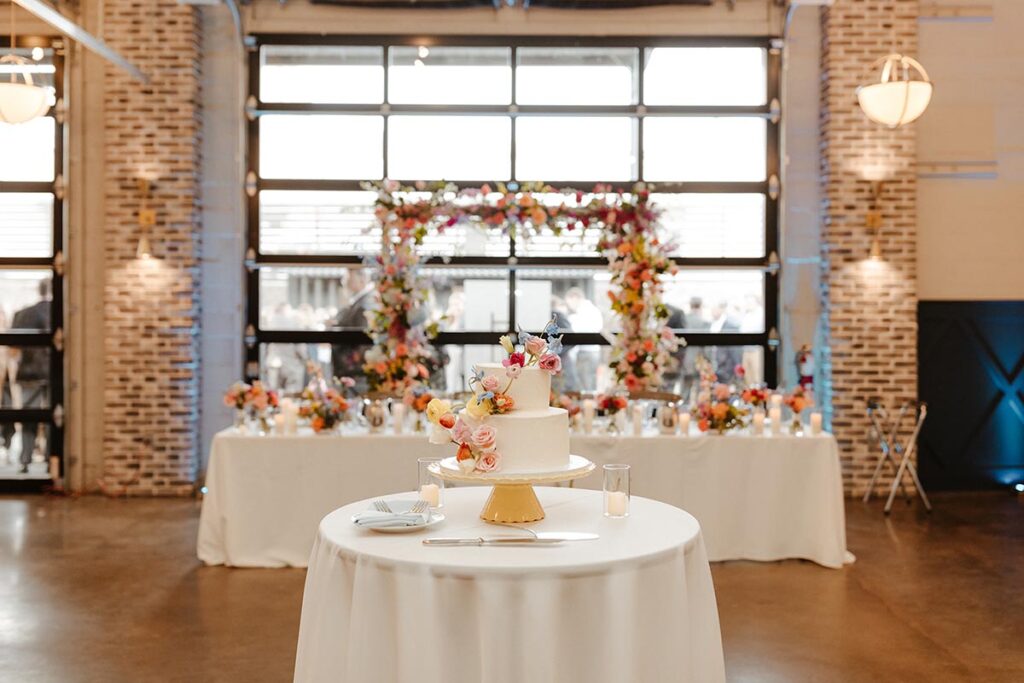 The wedding cake with cheerful flowers on top, and the head table covered in flowers in the background