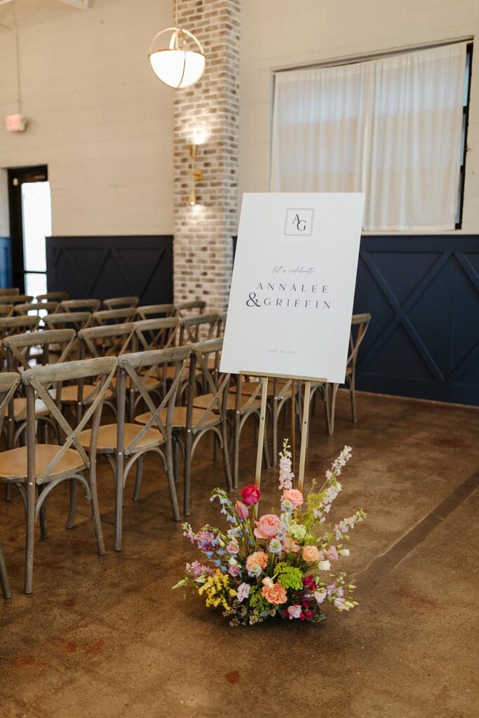 Ceremony welcome sign with large, colorful floral arrangment at the base