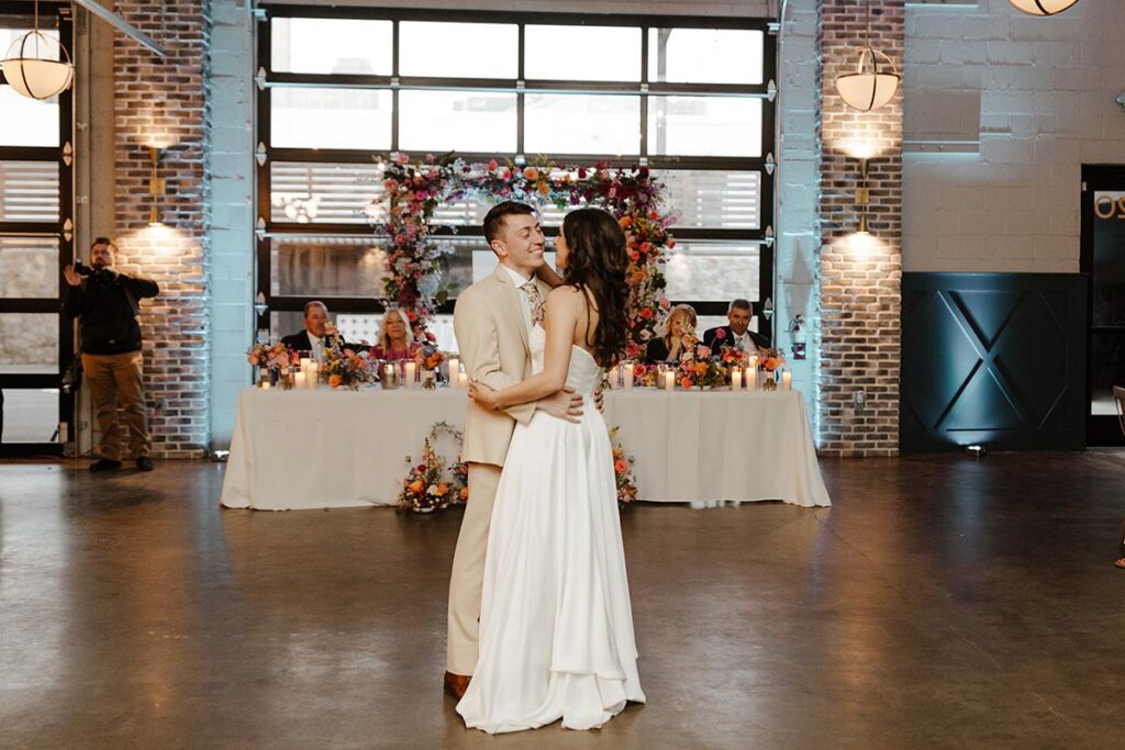 Couple sharing a first dance with floral heavy head table in the background.