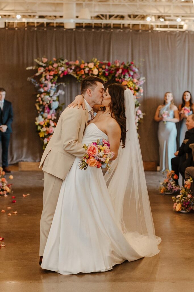 Bride and groom share kiss under the colorful full floral arbor