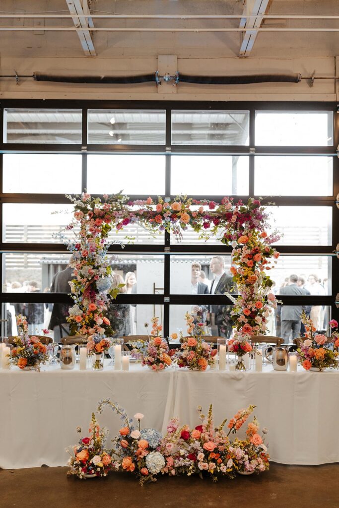 Head Table with floral arch behind it, flowers all over the top of it, and a wide floor arrangement in front of it