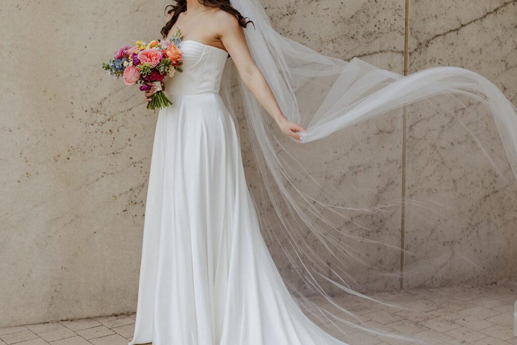 Bridal Dress detail with the veil flying in the wind as bride holds her colorful bouquet