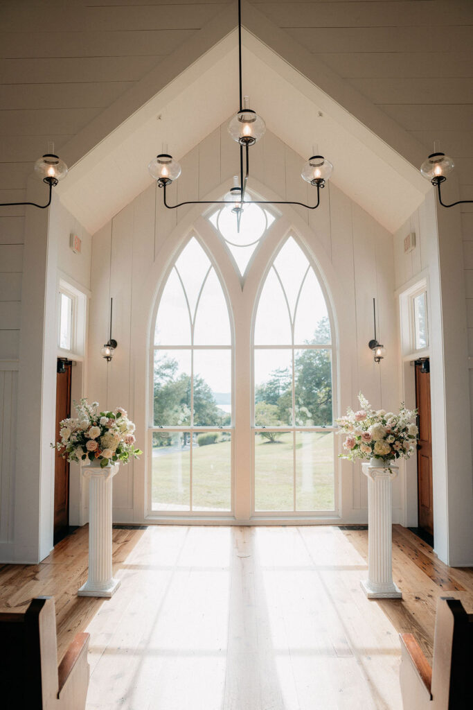 Two Coloums with large statement florals on top, in front of a large pointed chapel window