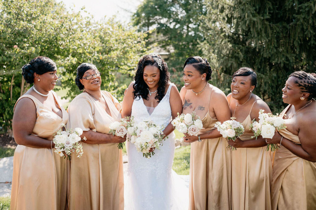 Bride with her bridesmaids in champagne dresses and white, blush, and taupe bouquets