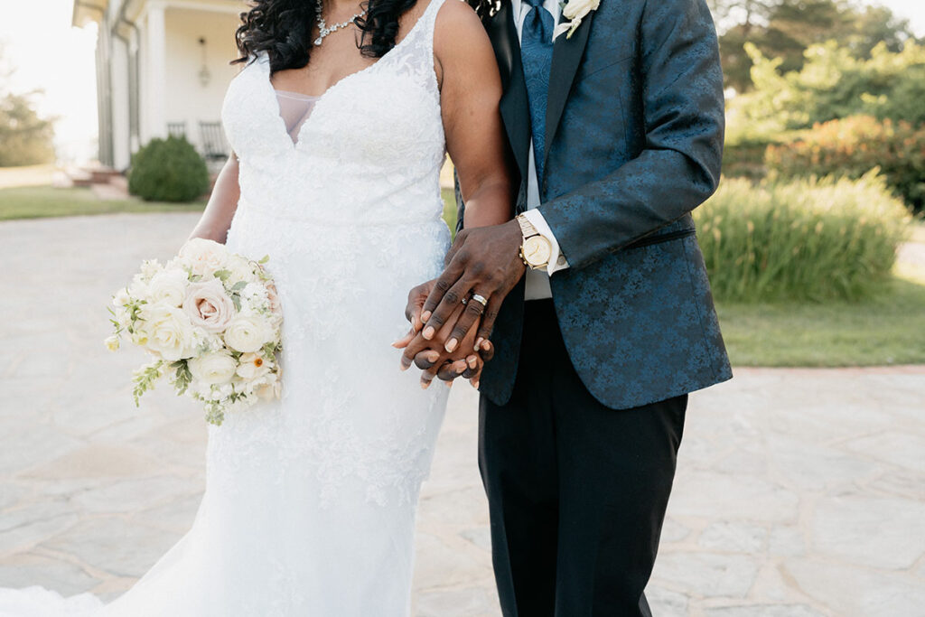 Close up of bride and groom holding hands and white bouquet