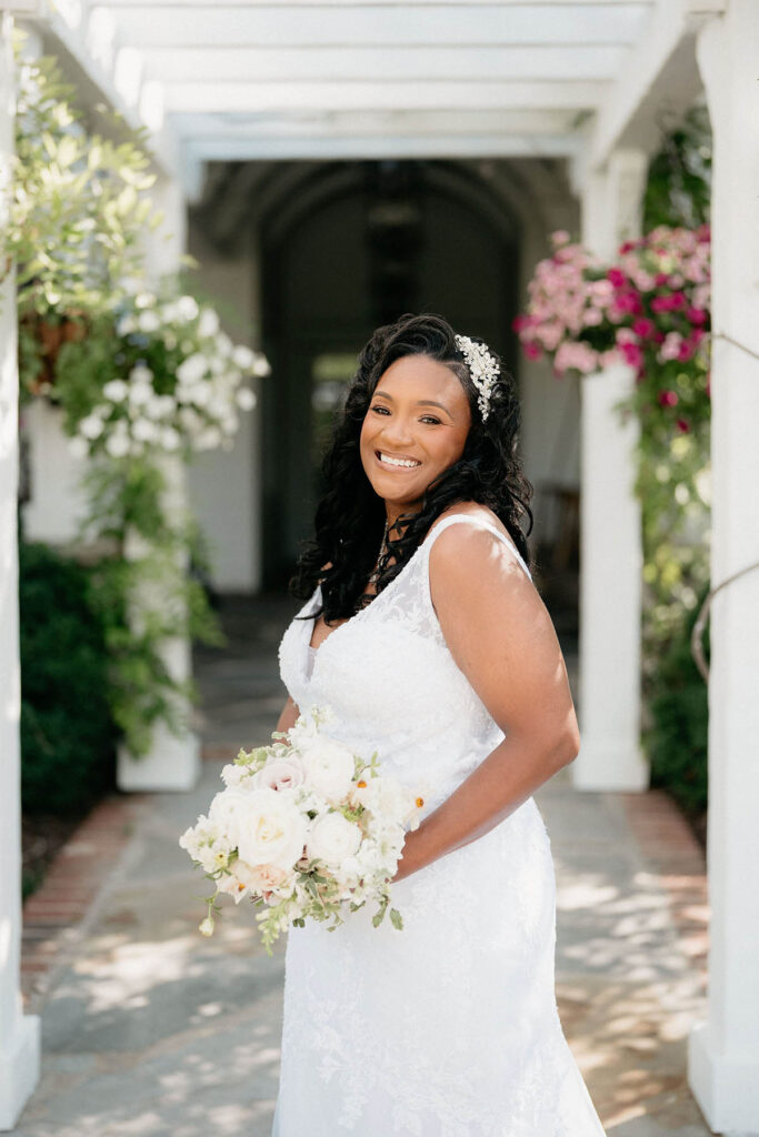 Bride smiling and holding bouquet with a shaded garden behind her