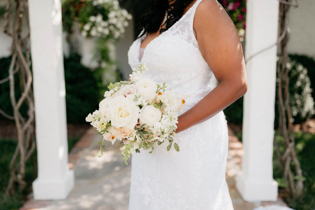 Close up of bride's dress detail and white, blush, and beige bridal bouquet